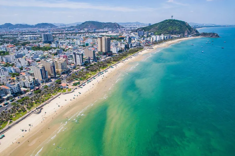 Aerial view of Vung Tau Back Beach curving along turquoise water with the Christ statue hill in the distance