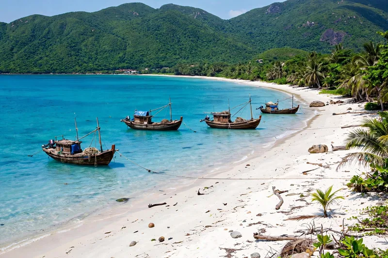 Con Dao bay with turquoise water, white sand beach, fishing boats and forested hills under a bright sky