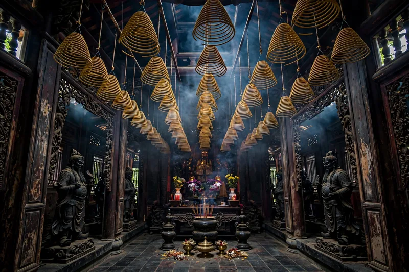 Hanging incense coils and carved wooden panels inside the dimly lit Jade Emperor Pagoda in Saigon