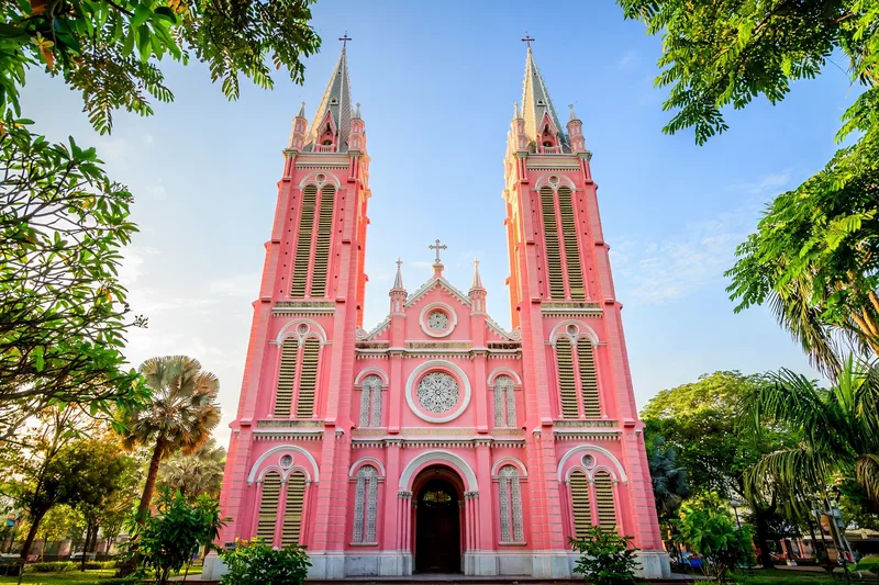 The pastel pink facade and twin bell towers of Tan Dinh Church glowing in bright morning sunlight