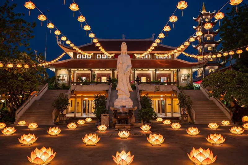 The tall seven story tower of Vinh Nghiem Pagoda rising above trees with worshippers in the courtyard (2)